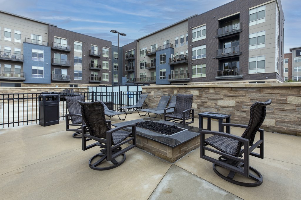 a patio with chairs and a fire pit in front of an apartment building