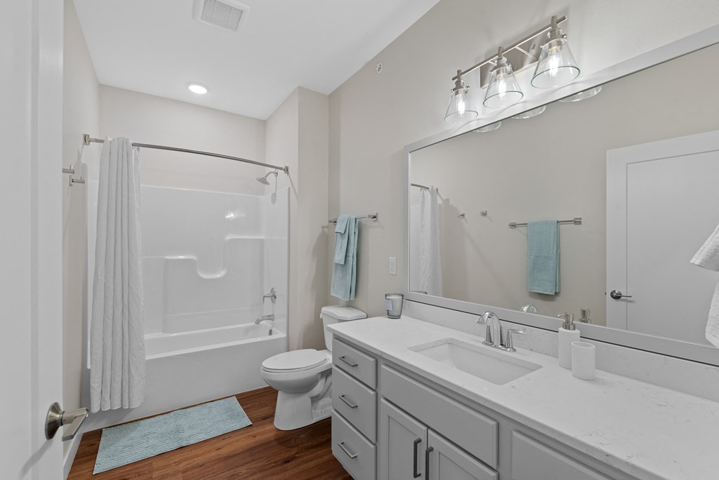 a white bathroom with a large mirror and a white toilet and shower at Tivoli Green Apartments & Townhomes, Mount Pleasant, WI