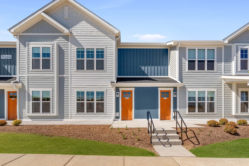 a row of houses with orange doors and blue siding at Tivoli Green Apartments & Townhomes, Mount Pleasant, WI