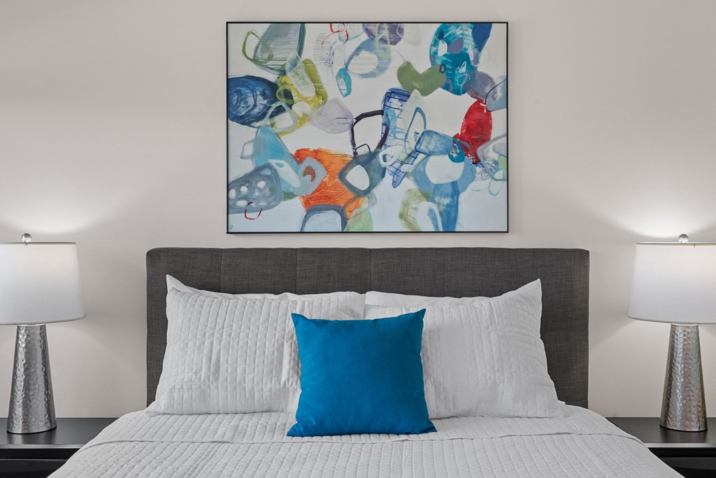 a bedroom with a bed with a blue pillow and a colorful painting above it at Tivoli Green Apartments & Townhomes, Mount Pleasant, WI