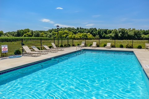 A swimming pool with lounge chairs and a fence.