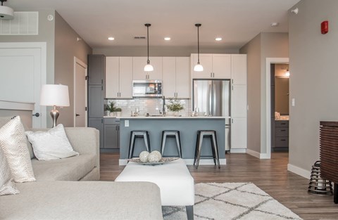 A modern living room with a grey sofa and a kitchen in the background.