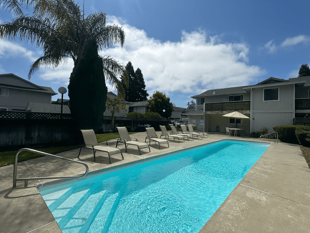 A swimming pool surrounded by chairs and trees.