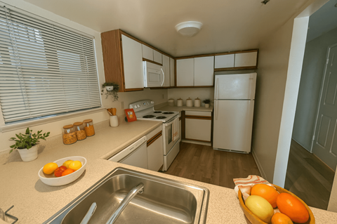 A kitchen with a white counter top and a bowl of fruit on it.