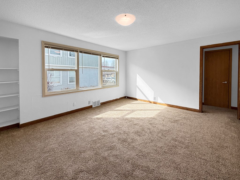 A room with a carpeted floor, a window, and a door.