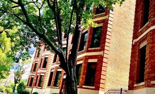 A tall building with red brick and white trim is surrounded by trees.
