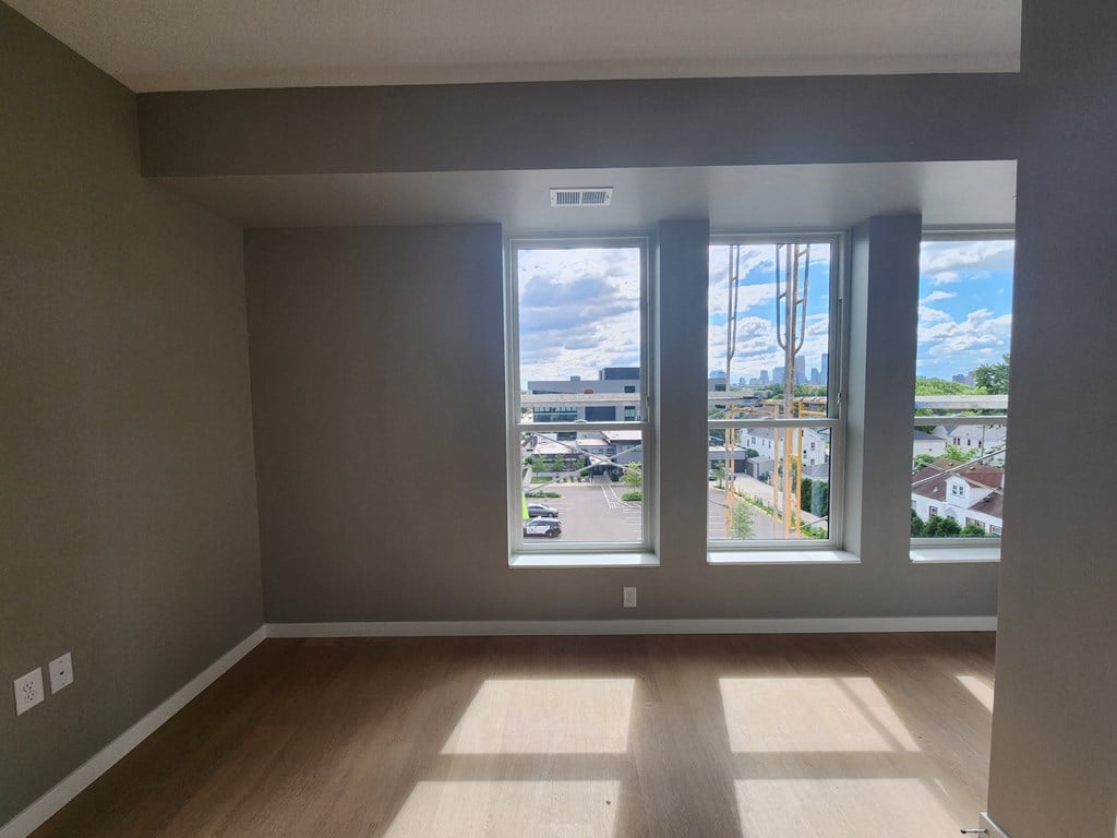 an empty living room with three windows and a city view