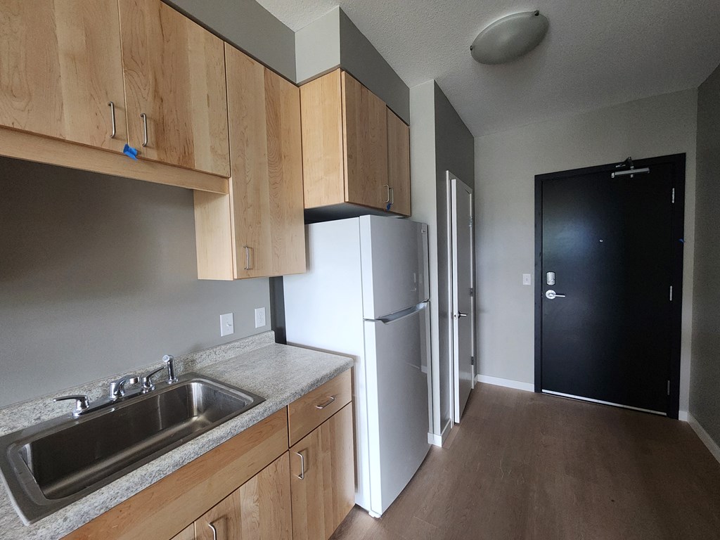 a kitchen with wooden cabinets and a refrigerator and a door to a hallway