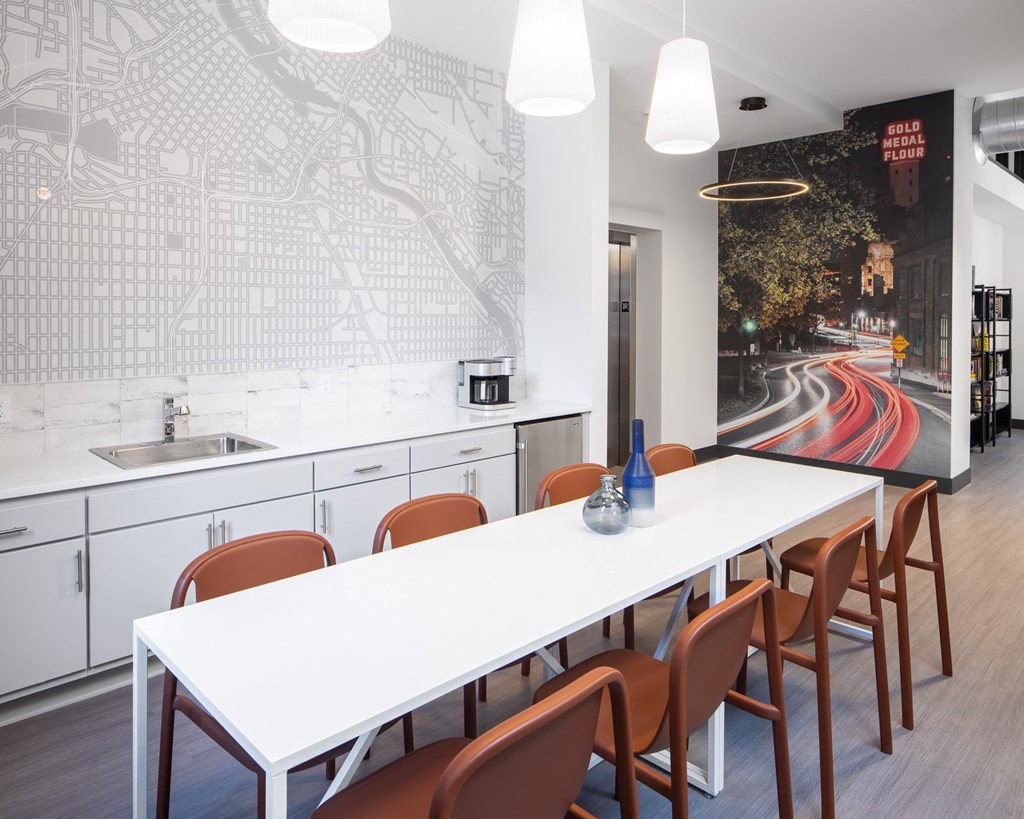 a long white table and chairs in a room with white cabinets and a wall mural