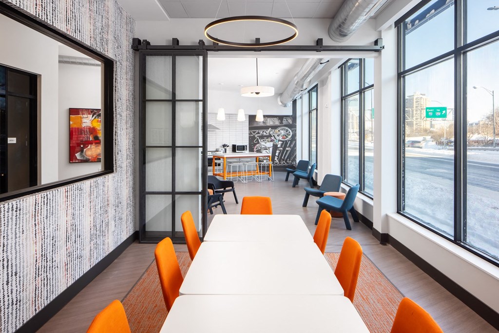 a long table with orange chairs in a room with large windows