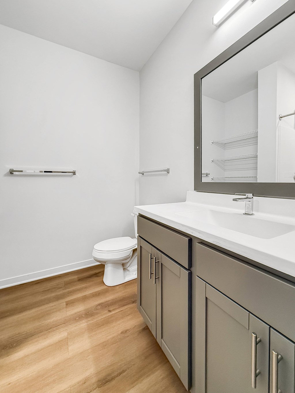 A white toilet sits in a bathroom with a wooden floor and a mirror above a sink.