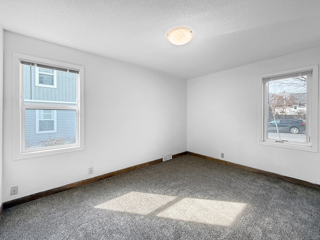 A bedroom room with a carpeted floor, two windows, and a ceiling light.