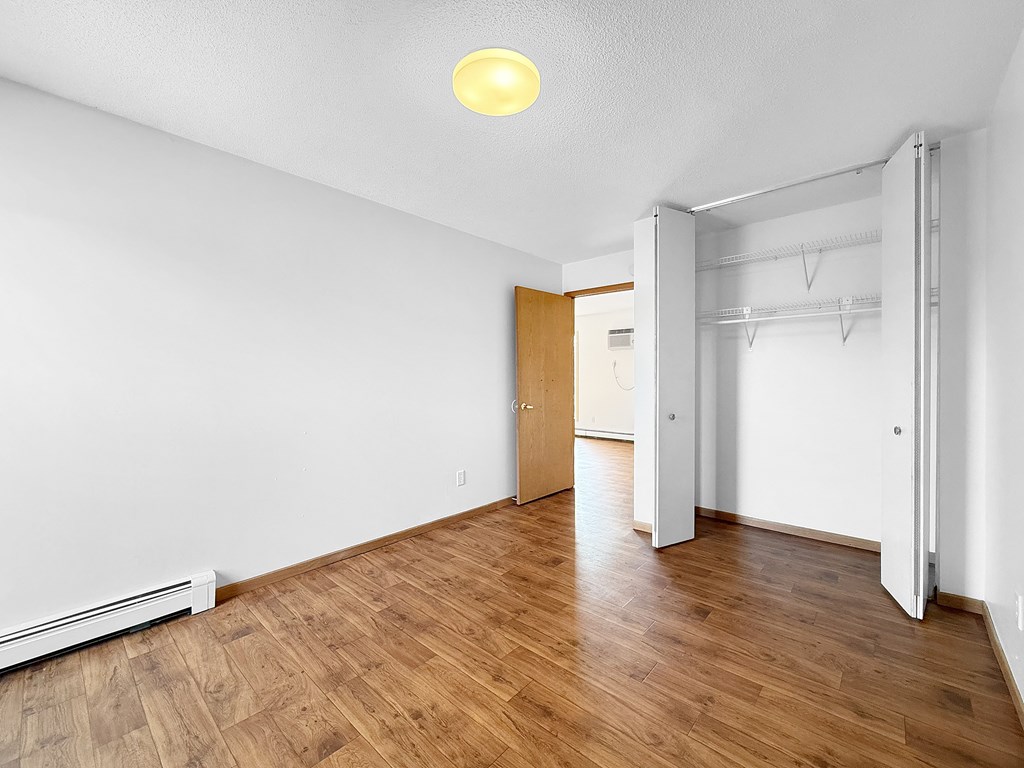 A room with a wooden floor and a white wall with a door and a window.