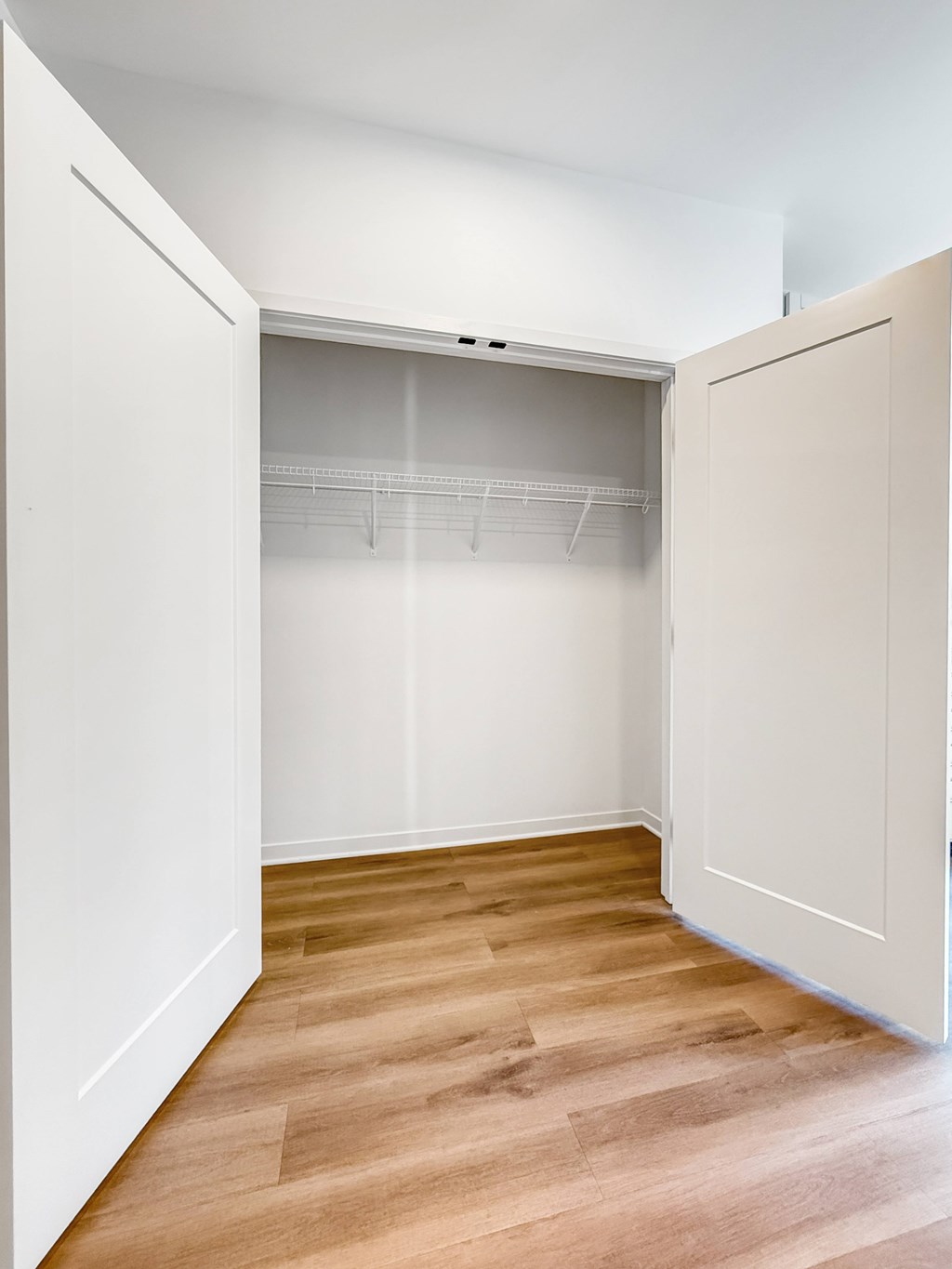 A white closet with a wooden floor and shelves.