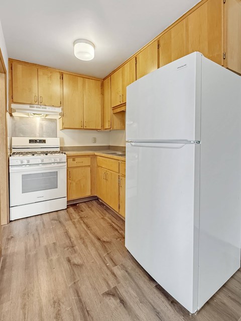 A white refrigerator stands in a kitchen with wooden cabinets.