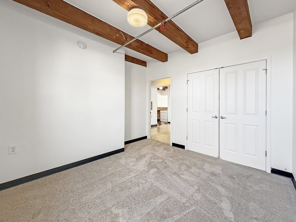 A room with white walls and a carpeted floor with a wooden beam ceiling.