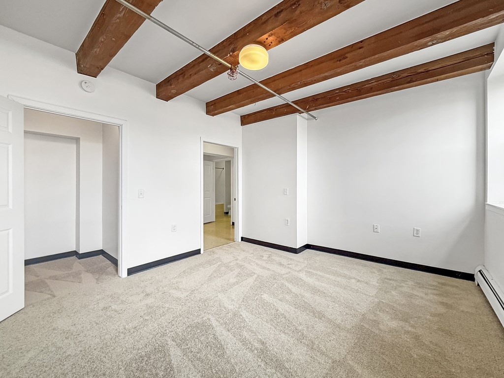 A room with a carpeted floor and wooden beams on the ceiling.