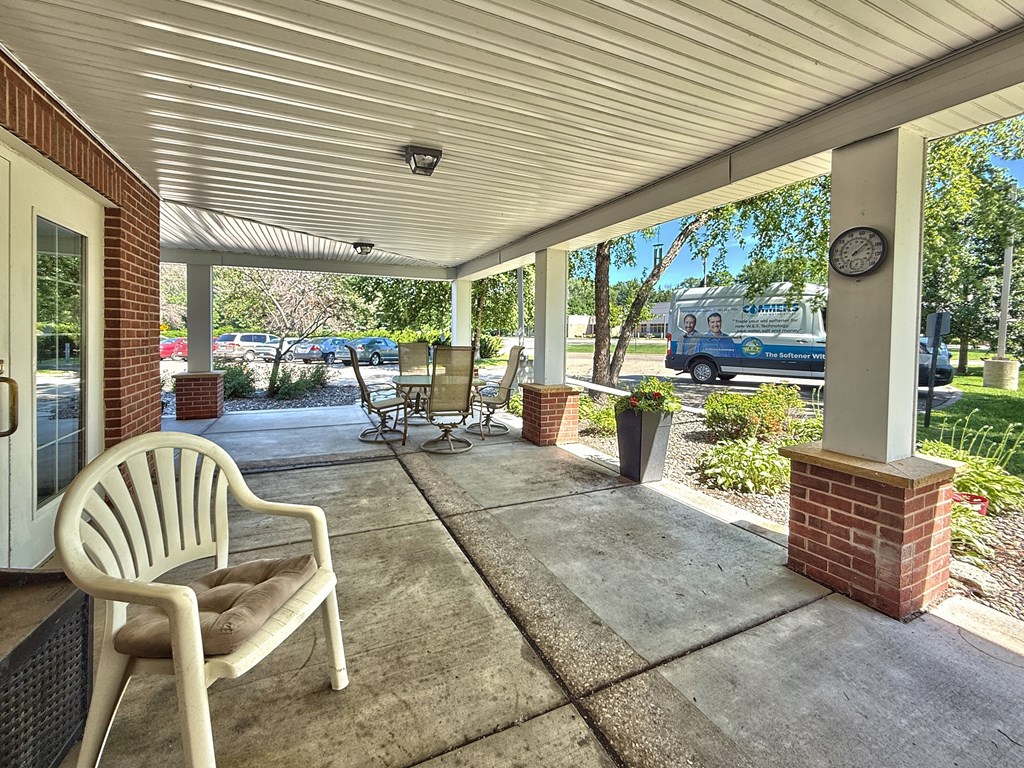 A white chair is on a porch with a clock on a post.