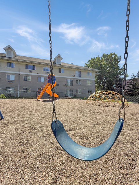 A swing set in a playground with a blue slide.