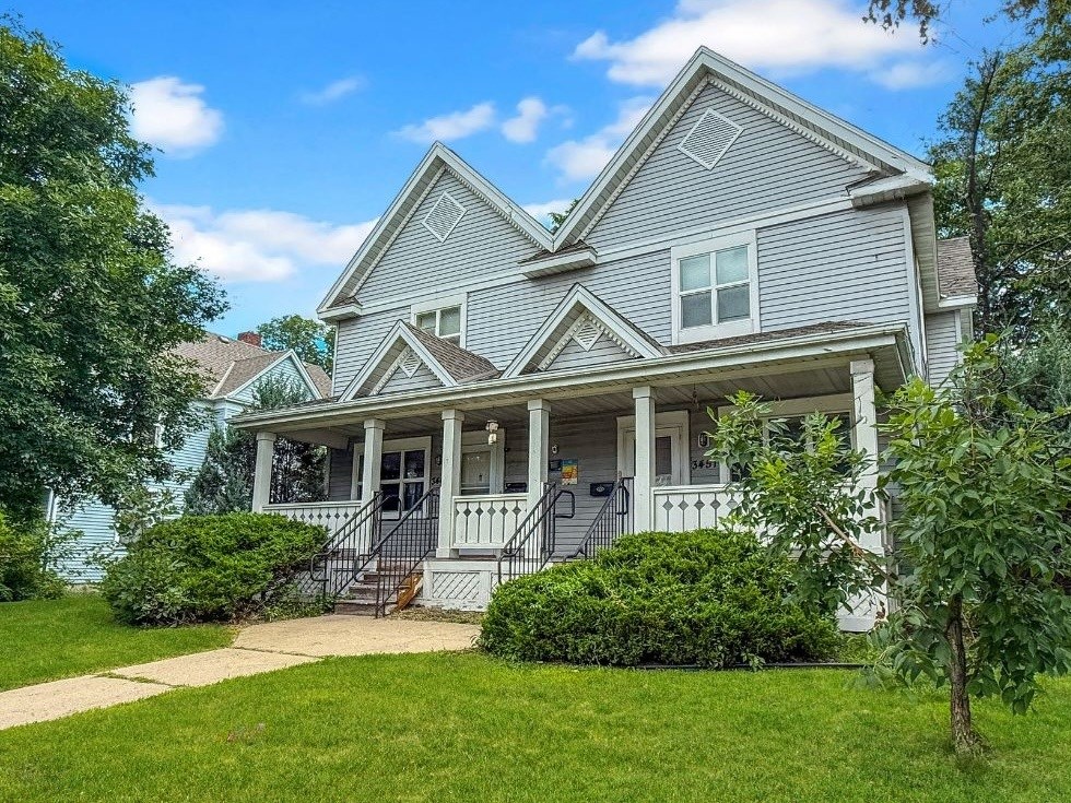 A two-story house with a front porch and a tree in front.