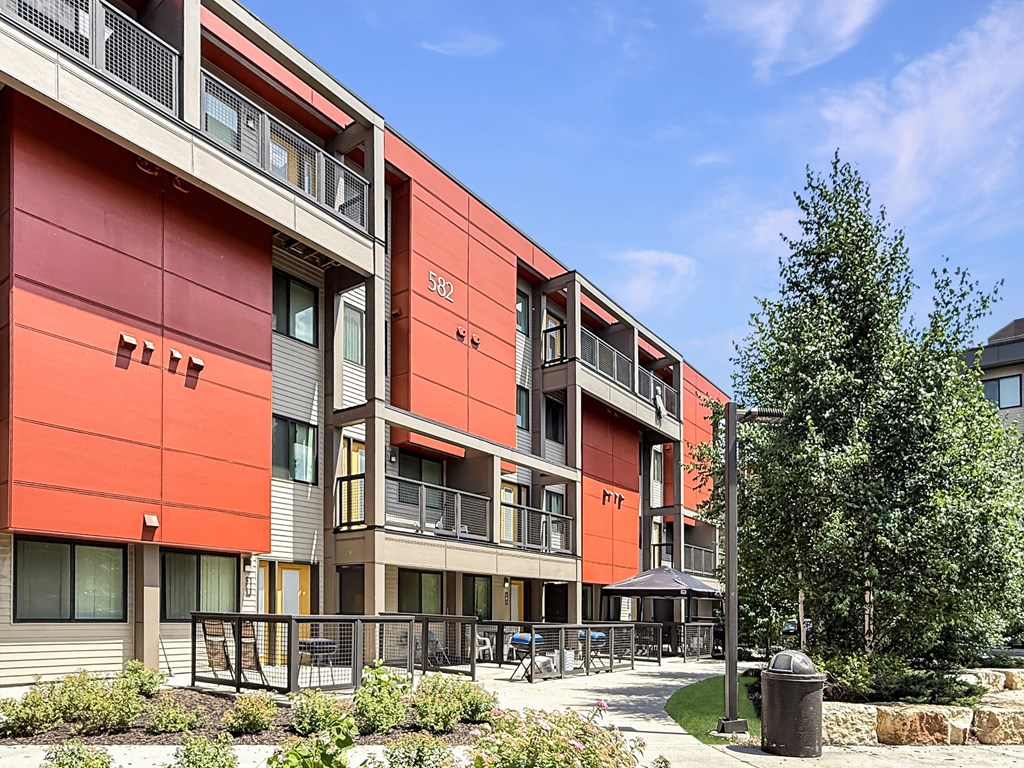 A modern building with a red and beige exterior and a courtyard in front.