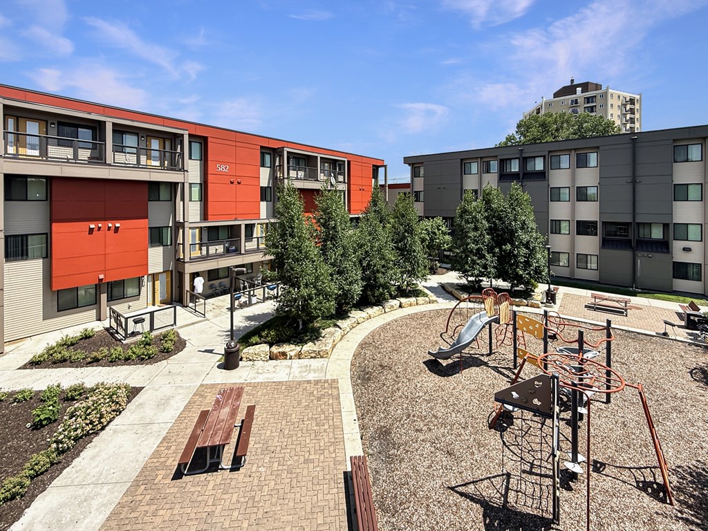 A playground with a slide and a play structure in the foreground and apartment buildings in the background.