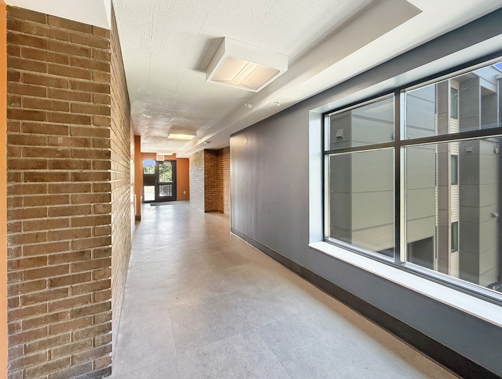A long hallway with brick walls and windows on the side.