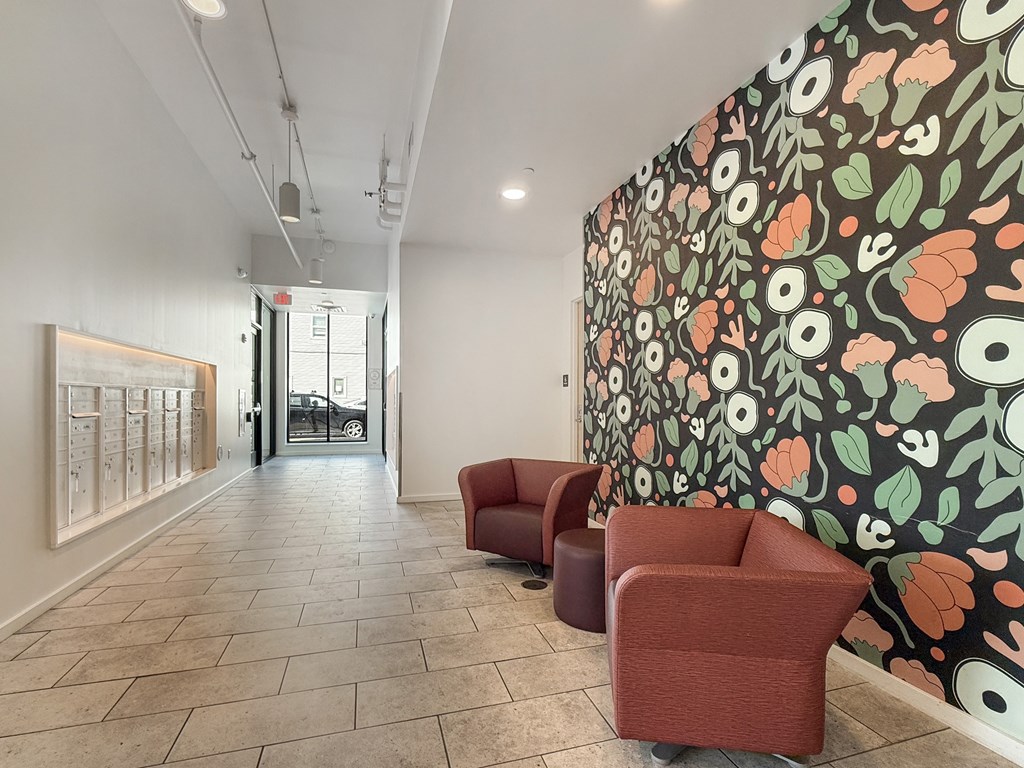 A hallway with a wallpapered wall and two red chairs.