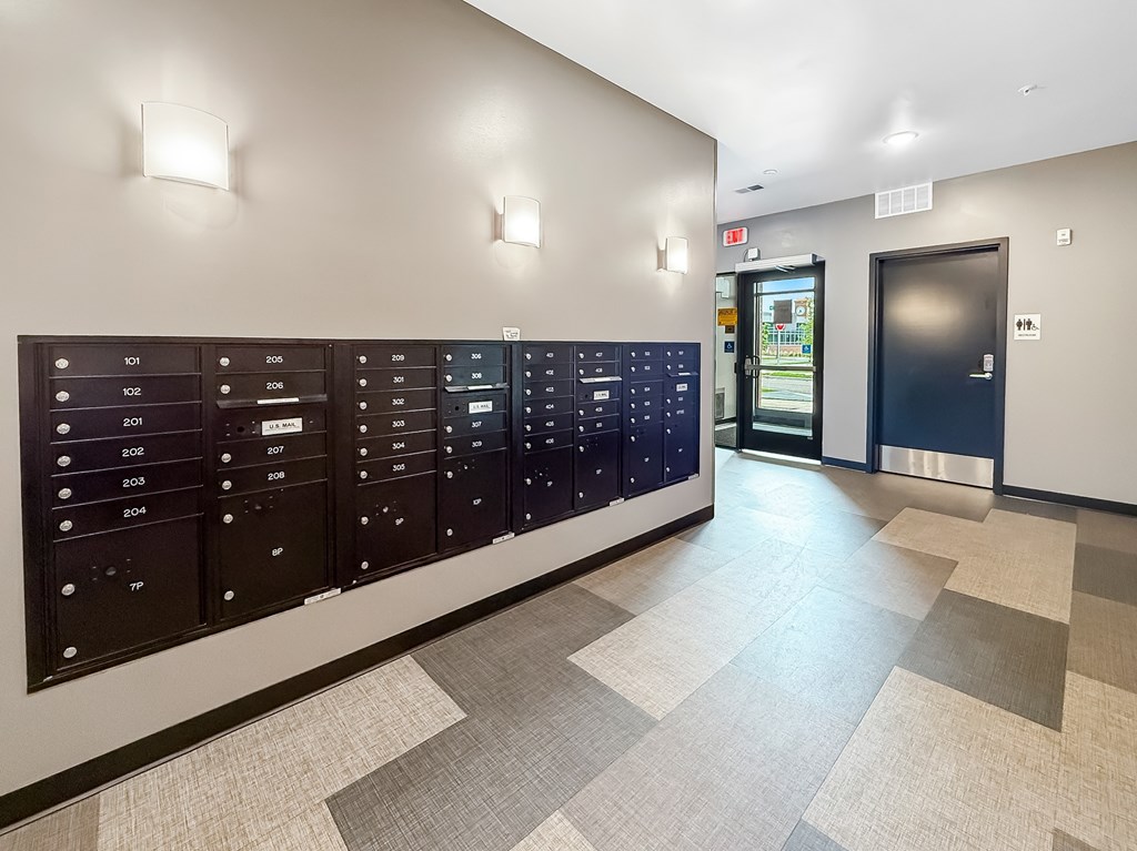 A hallway with a wall of mailboxes and a door at the end.