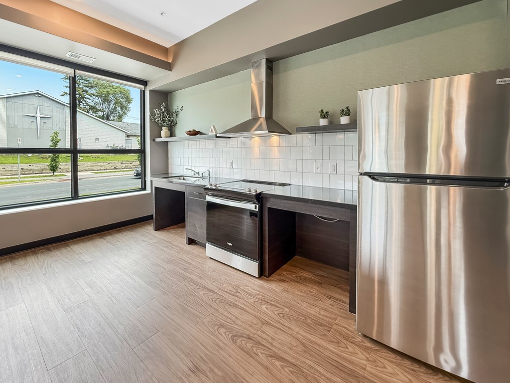 A modern kitchen with a stainless steel refrigerator and wooden flooring.
