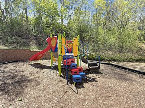 A playground with a red slide, a blue and yellow climbing frame, and a red and blue climbing wall.
