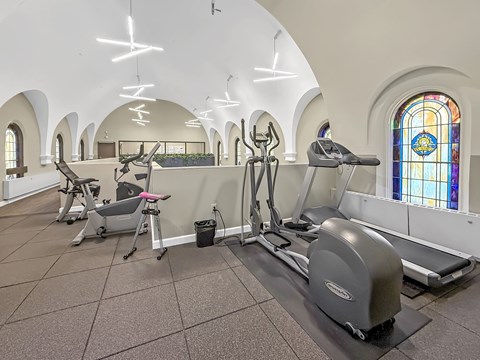 A gym with exercise equipment and stained glass windows.