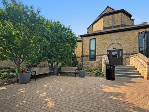 A brick building with a black door and windows is surrounded by trees and benches.