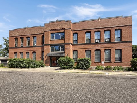 A red brick building with a black awning and a parking lot in front.