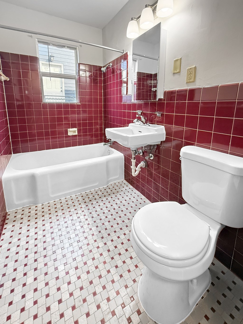A vintage bathrom with dark red tiles, white toilet, a floating sink, and tub/shower