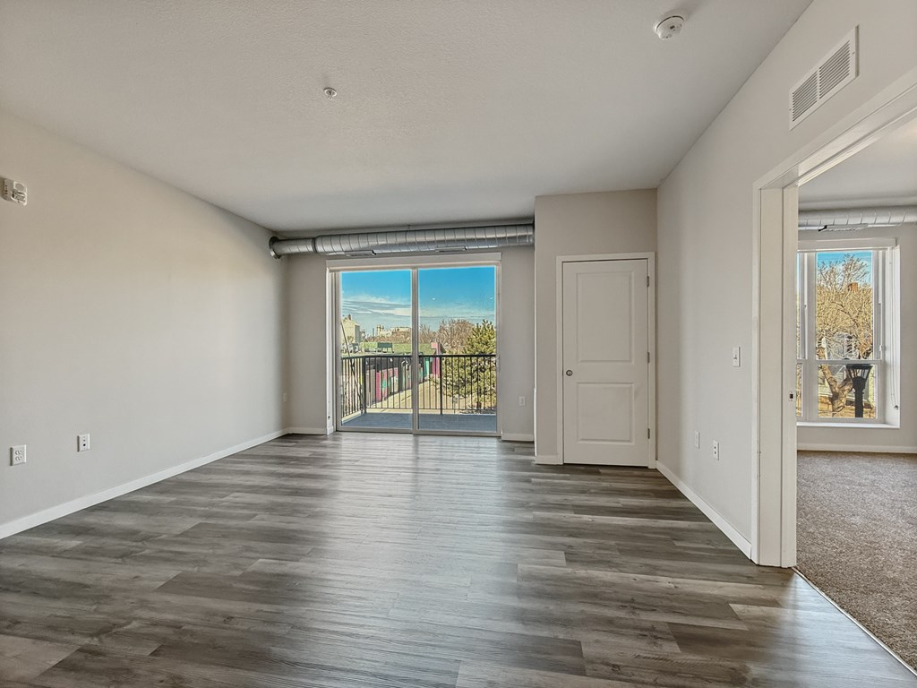 A spacious room with wooden flooring and a view of a fenced area outside through a sliding glass door.