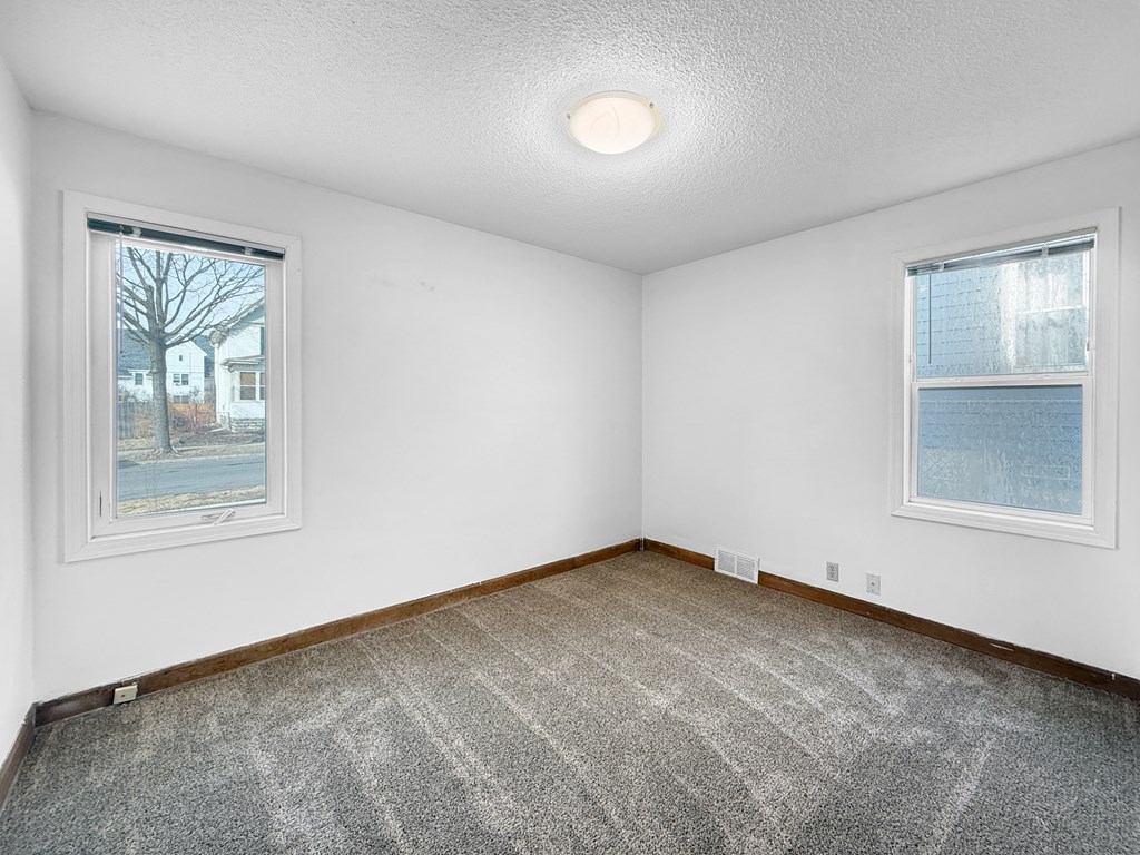 A room with a carpeted floor and two windows.