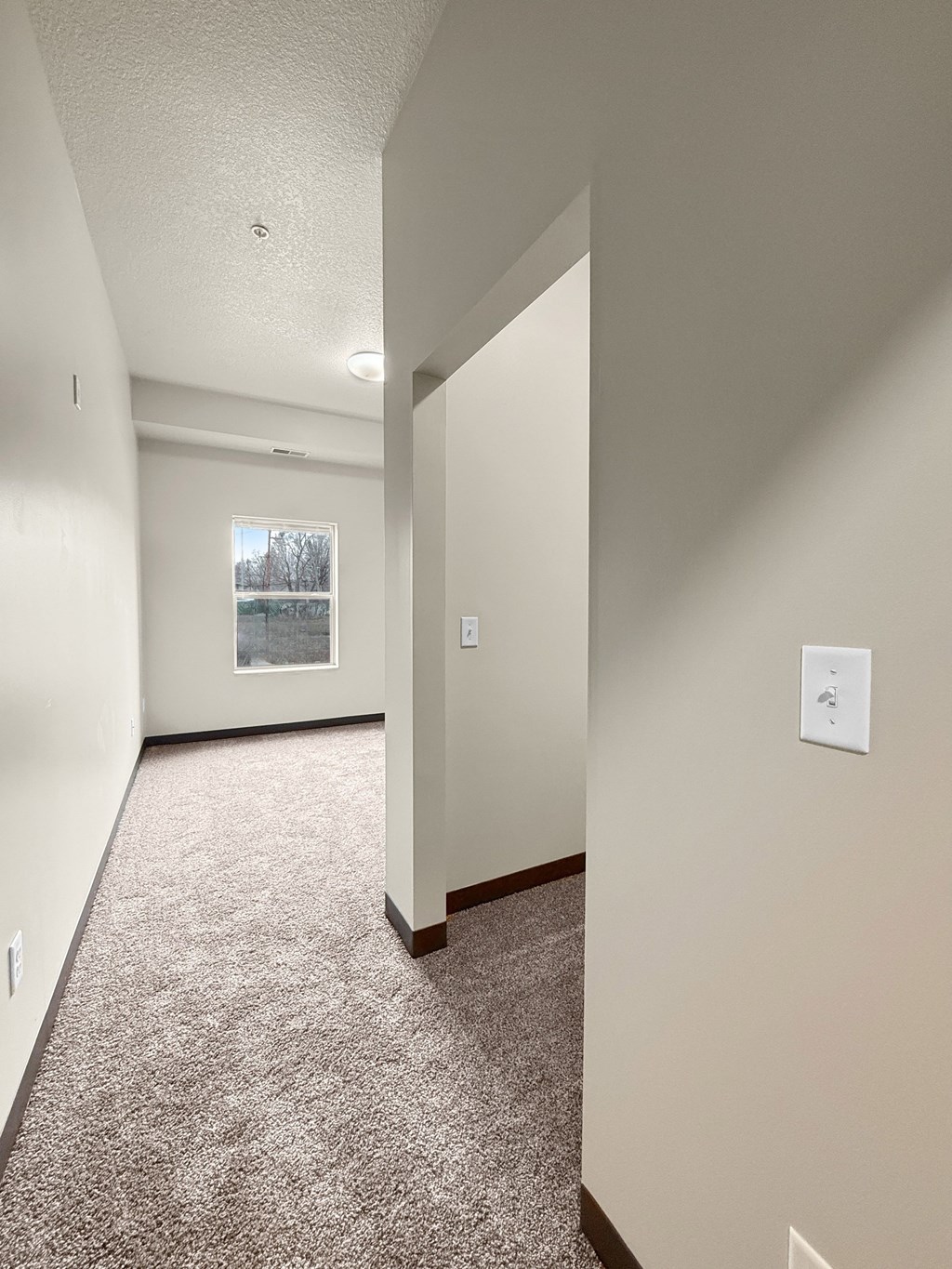 A view of a bedroom hallway leading to walk in closet and a window at the end