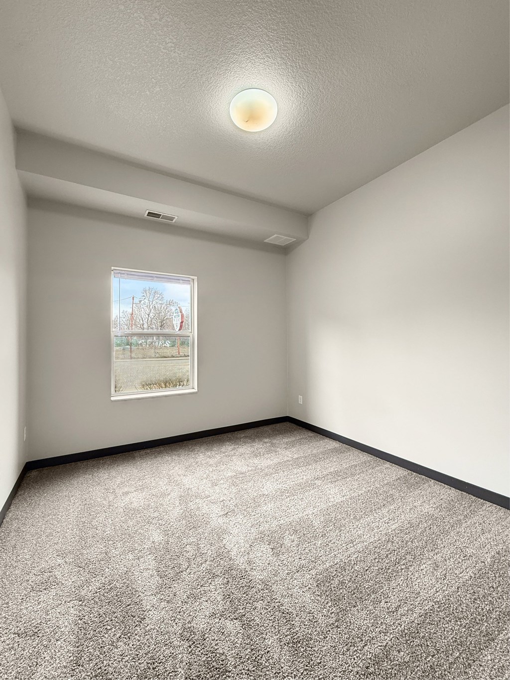 A bedroom room with a grey carpet and a window looking outside
