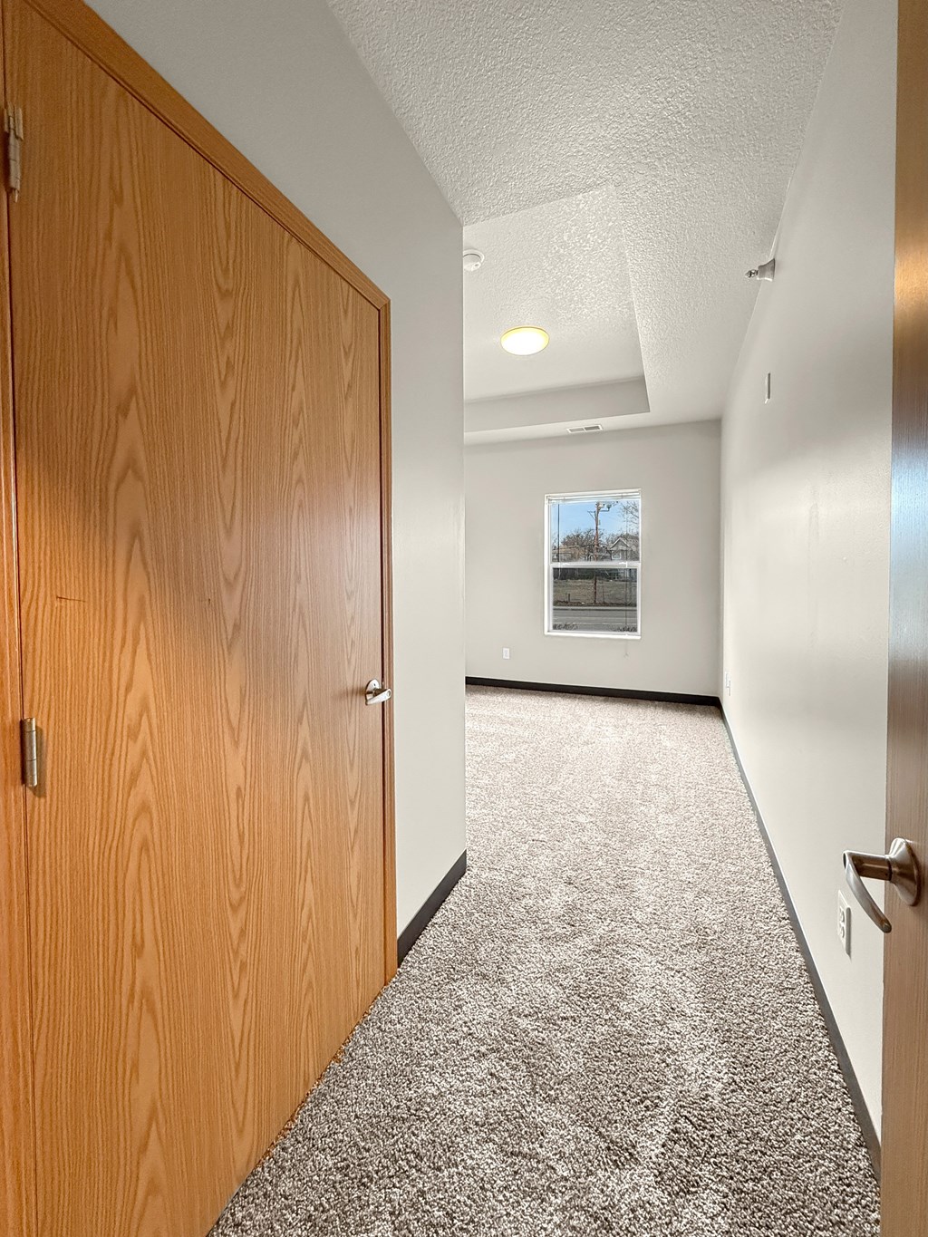 Another bedroom with a small hallway, closet door to the side and a window at the end of the room