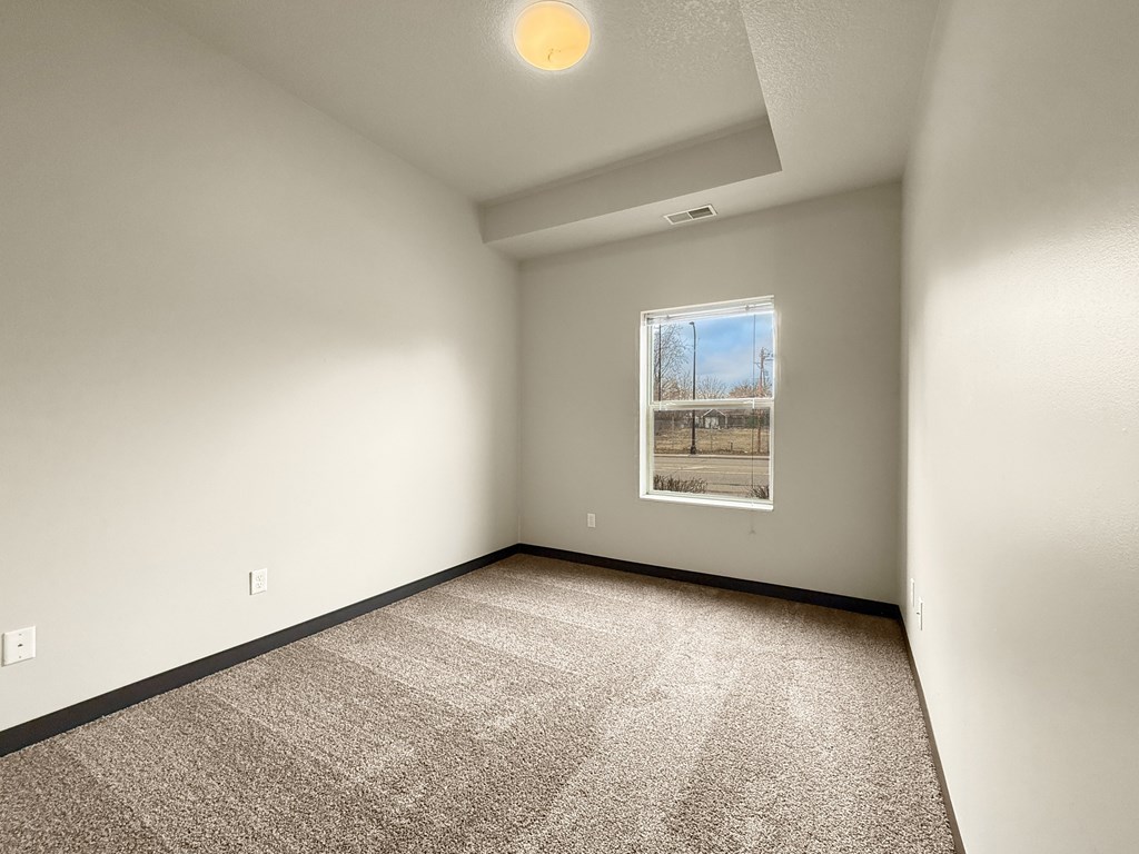 a second bedroom with carpeted floor and a window showing outside.