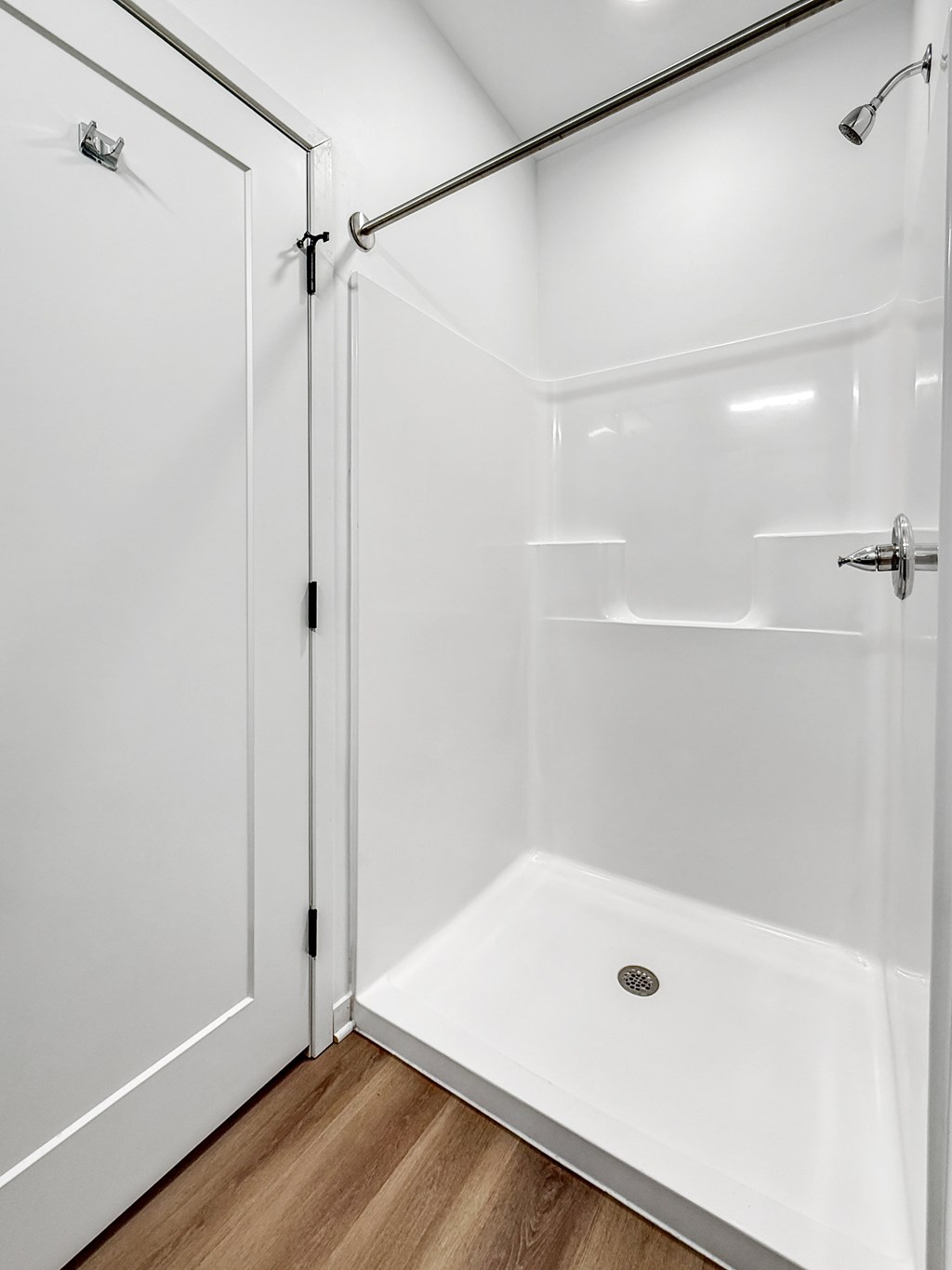 A white bathroom with a walk-in shower and a white door.