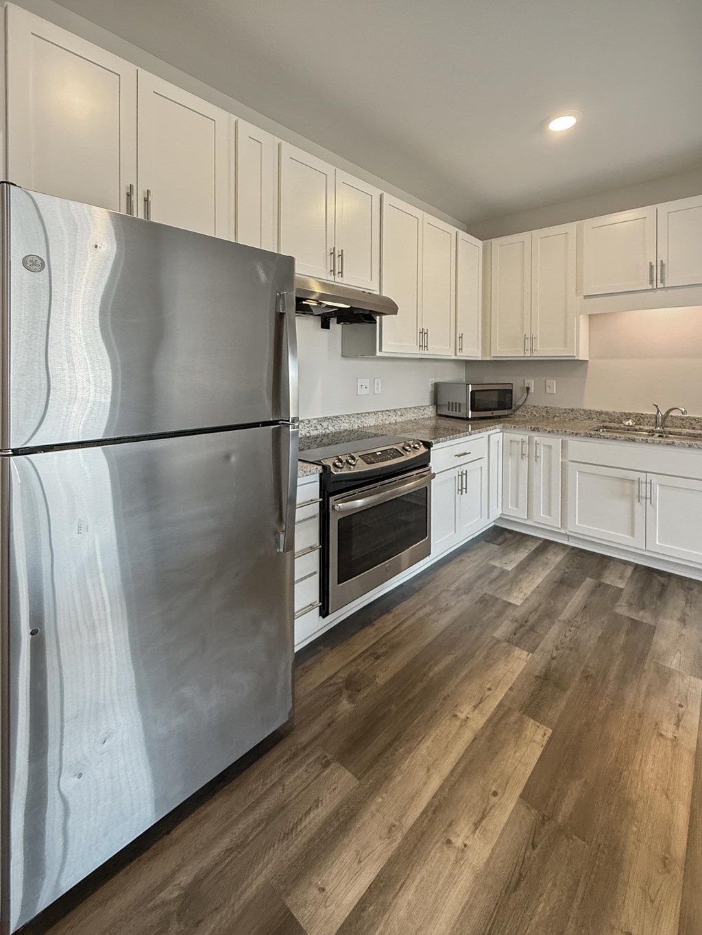 A kitchen with a stainless steel refrigerator and wooden floors.