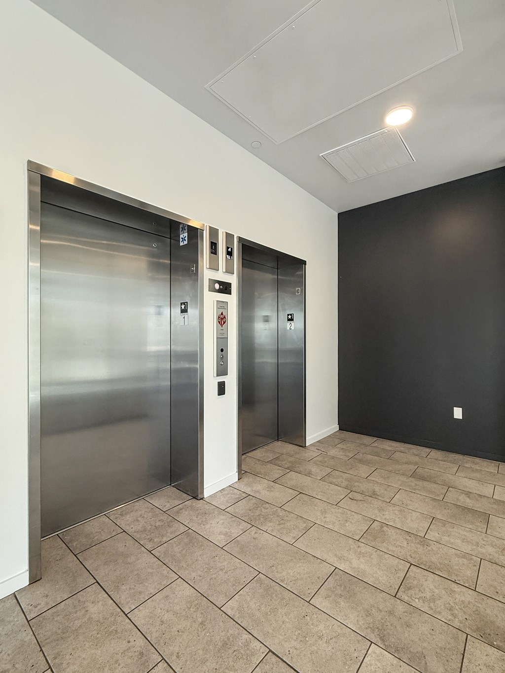 Two stainless steel elevators in a hallway with tiled flooring.