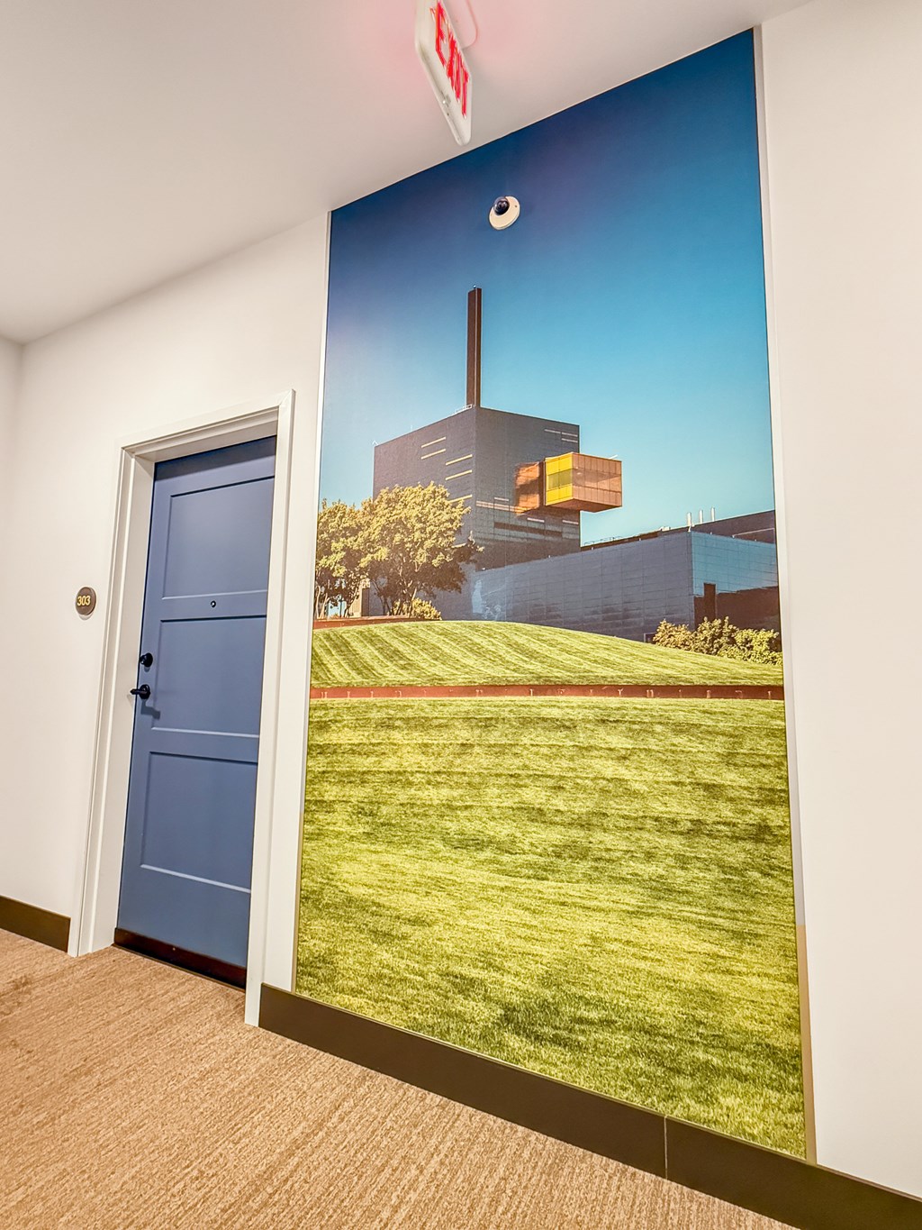 A wall mural depicting a building and a field with a blue door in the foreground.