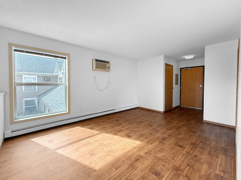 A room with wooden flooring and a window showing a house across the street.