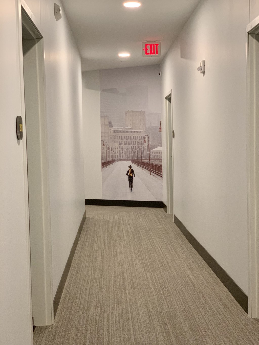 a person walking down a hallway with an exit sign on the wall