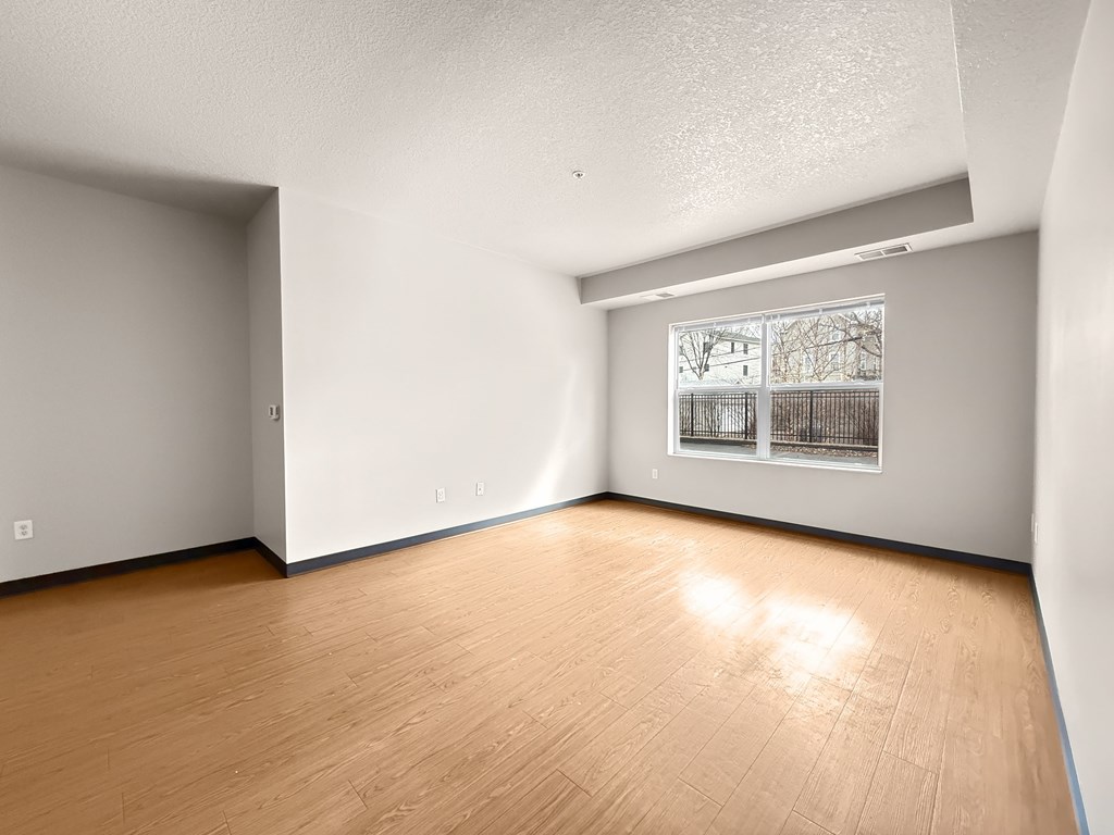 A room with wooden flooring and a window with bars on it.