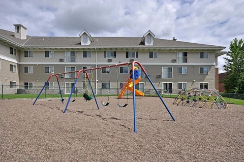 A playground with swings and slides in front of a building.