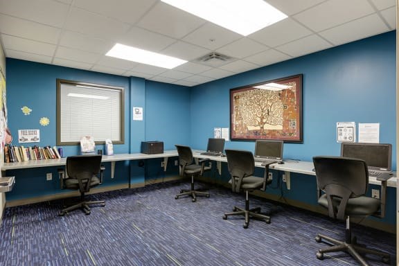 A room with blue walls and a carpeted floor has several chairs and desks arranged in rows.